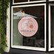 Vitrine de magasin avec autocollant de signalétique circulaire, personnalisée pour "Emily Beauty Cosmetics". Design minimaliste avec illustration florale sur fond rose pâle, positionnée sur une grande fenêtre en verre. Idéal pour les commerces et artisans cherchant une vitrine attrayante et moderne.