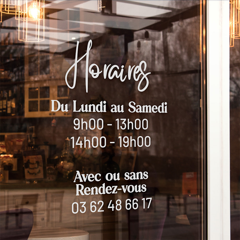 Vitrine de magasin avec signalétique indiquant les horaires d'ouverture, du lundi au samedi, de 9h00 à 13h00 et de 14h00 à 19h00, avec option de rendez-vous, en lettres blanches sur fond transparent.